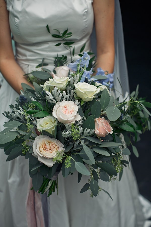 Bride holds large wedding bouquet made of greenery and white roses
